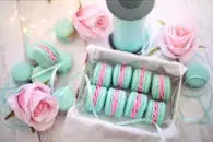 A delightful display of pastel macarons with pink roses and teal ribbons.